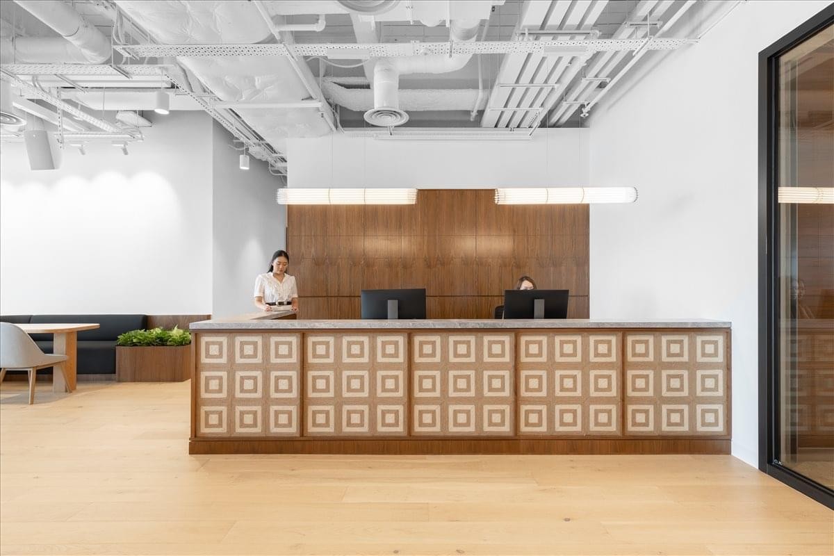 Bright reception area at Hysan Place with a patterned wooden desk and exposed ceiling pipes.