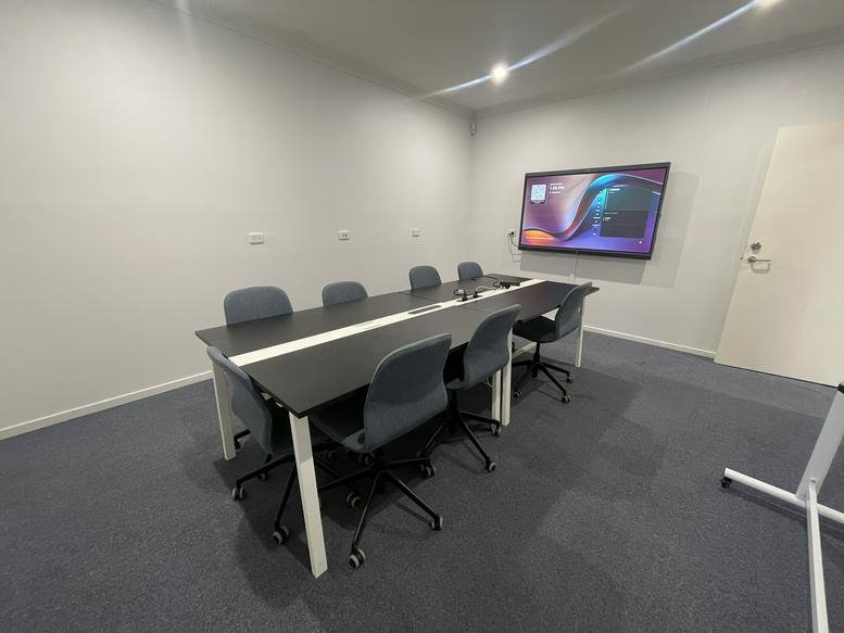 Meeting room with a long dark table, grey chairs, and a large wall-mounted screen.