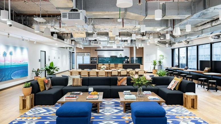Expansive open-plan communal hub with modular seating, blue rugs, and exposed ceilings.