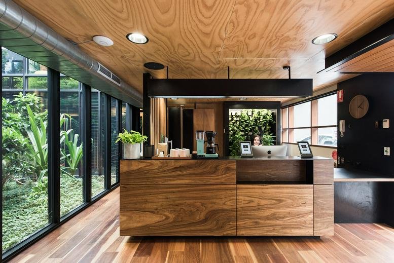 Reception area at 36-38 Gipps Street with a warm wood-panelled desk, matching ceiling, and floor-to-ceiling windows.
