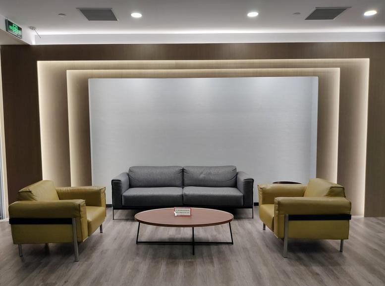 Sleek modern lounge at Lihpao Plaza with yellow armchairs and a grey sofa against a tiered backlit wall.