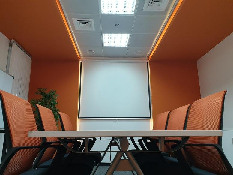 Spacious boardroom with orange feature walls and a large screen at Mazaya Business Avenue AA1.