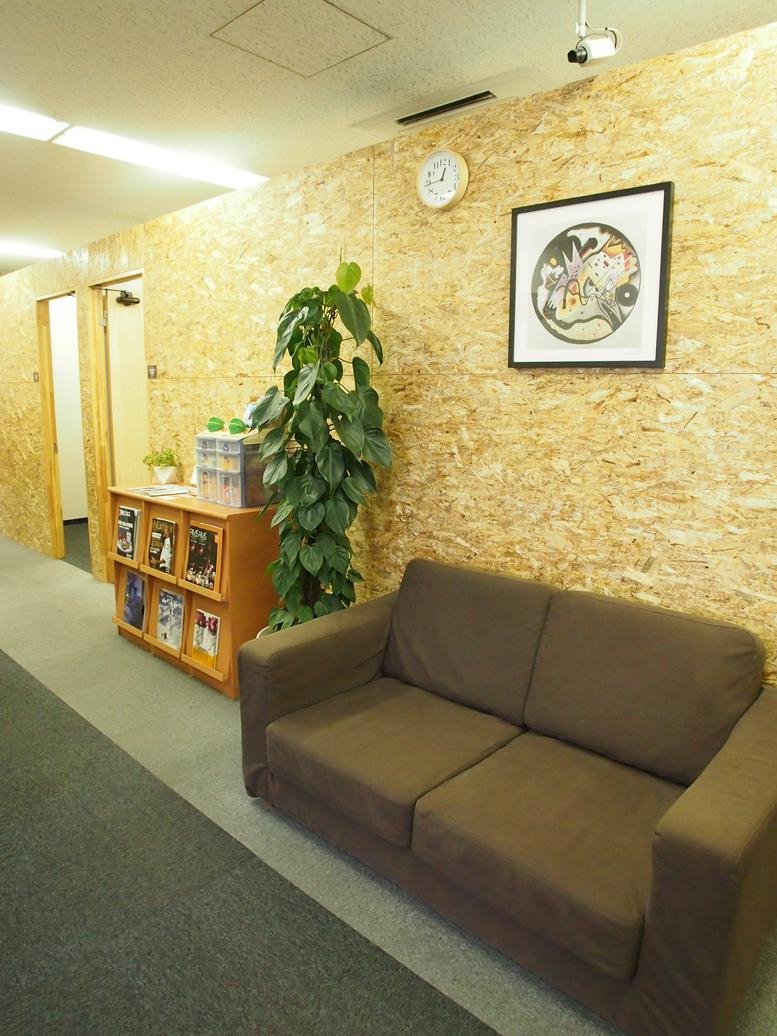 Warm communal lounge area with wood-chip walls, a brown sofa, and a tall green plant.