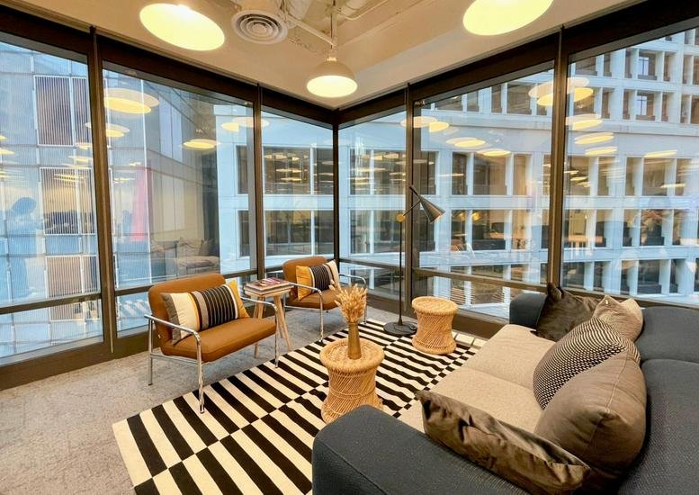 Stylish breakout area with a striped rug, leather armchairs, and floor-to-ceiling city views.