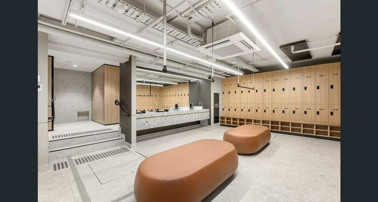 Spacious change room area with tan leather benches and rows of light wood lockers.