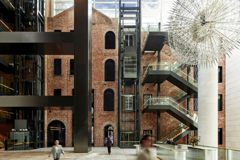 Spacious modern lobby at 477 Collins Street featuring a historic brick facade, glass elevators, and art installation.