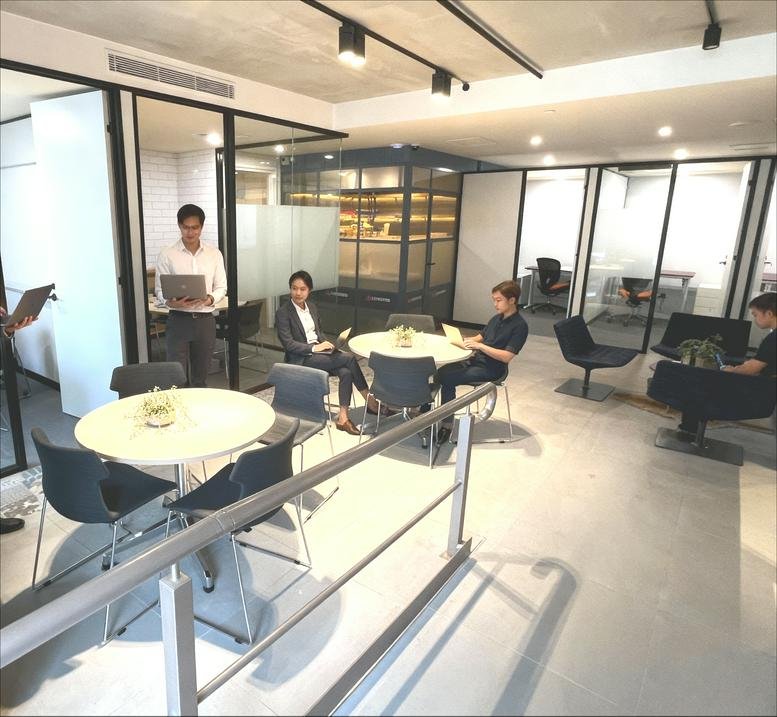 Bright coworking lounge with people working at round tables near glass partitions.