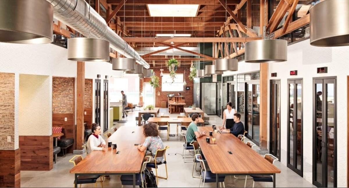 Spacious communal coworking area at Spectrum Tower with long wooden tables and industrial ceiling detail.