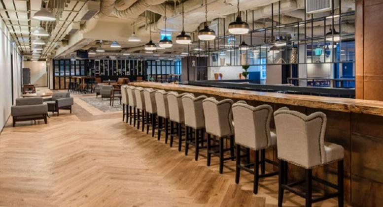 Spacious lounge at Champion Tower with a long wooden bar, herringbone floors, and industrial lighting.