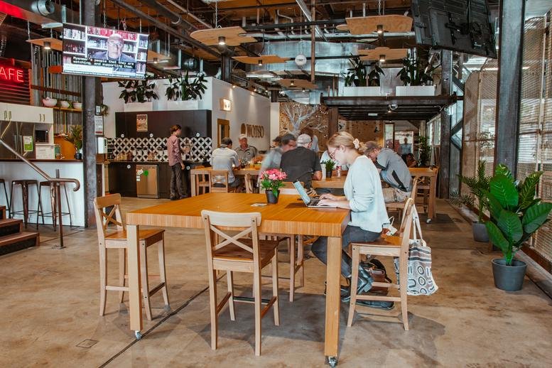 Cafe and coworking area at 5 George Street with high tables, wooden chairs, and industrial ceiling.
