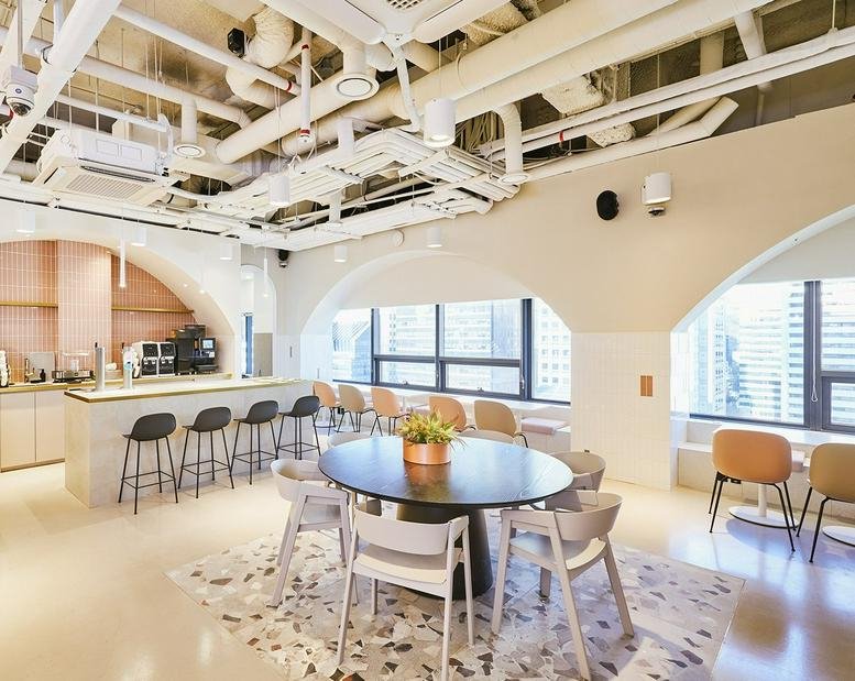 Bright coworking area with a central round wooden table and arched windows overlooking the city.