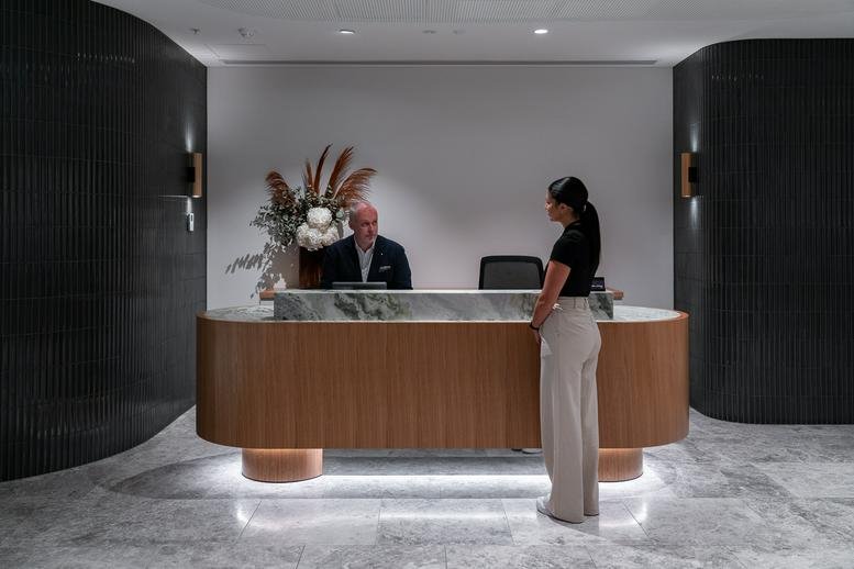 Sleek wooden reception desk with marble accents and a warm lighting feature at 555 Collins Exchange.