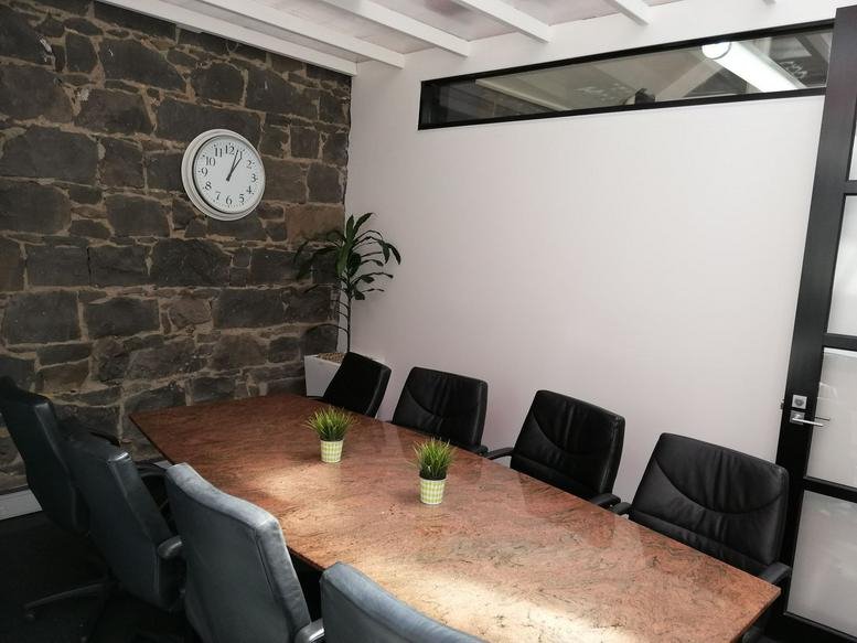 Boardroom with a long wooden table, black leather chairs, and an original stone feature wall.