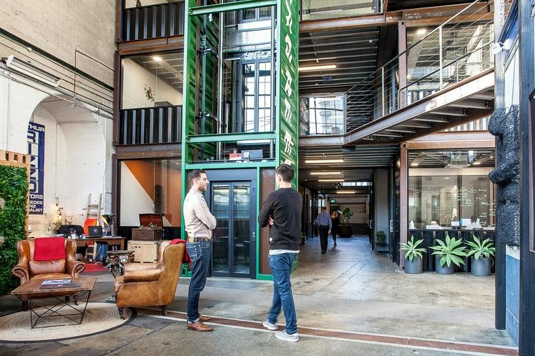 Spacious industrial lobby with high ceilings, a green elevator shaft, and leather lounge seating.