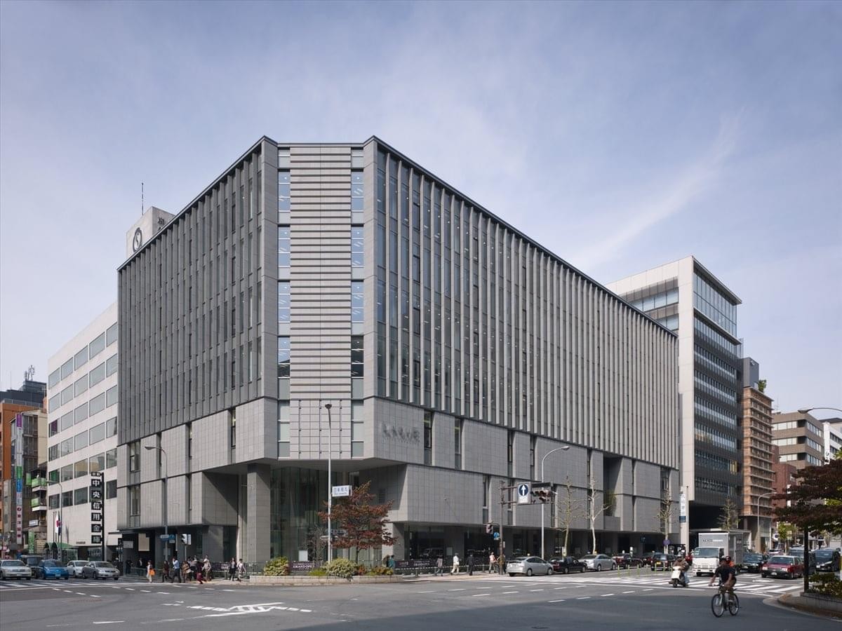 Modern grey facade of the Urbannat Shijyokarasuma Building with large glass windows and street-level shops.