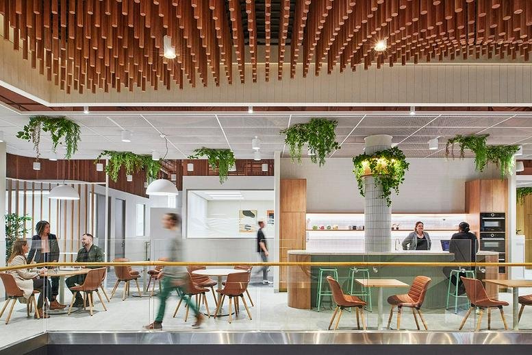 Spacious communal lounge and cafe at 793 Burke Road, Camberwell Place with wood-slat ceiling and greenery.