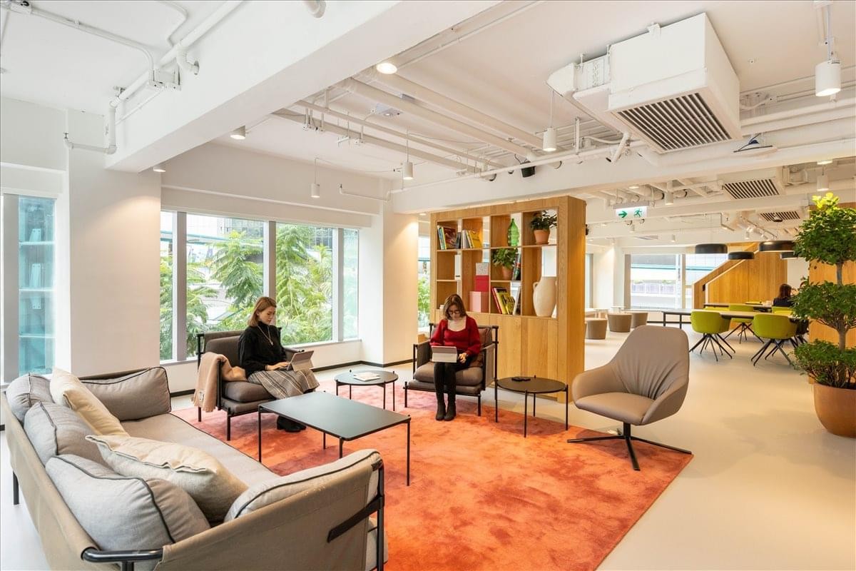 Spacious communal lounge with plush seating, orange rug, and floor-to-ceiling windows.
