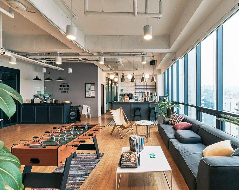Spacious coworking lounge with a foosball table, blue sectional sofa, and floor-to-ceiling city views.
