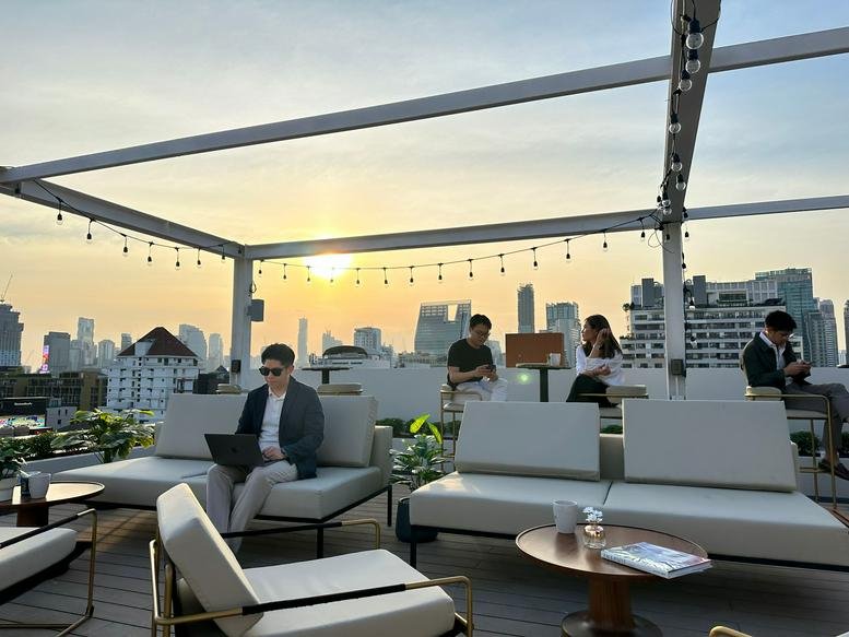 Rooftop terrace lounge with comfortable white sofas and a stunning city skyline view at sunset.