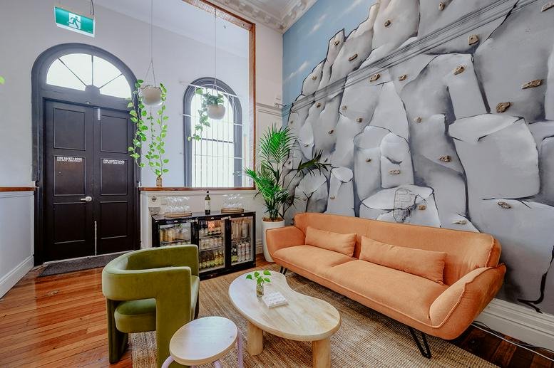 Lounge area at 84A Brunswick Street with an orange sofa, green armchair, and large rock-texture mural.