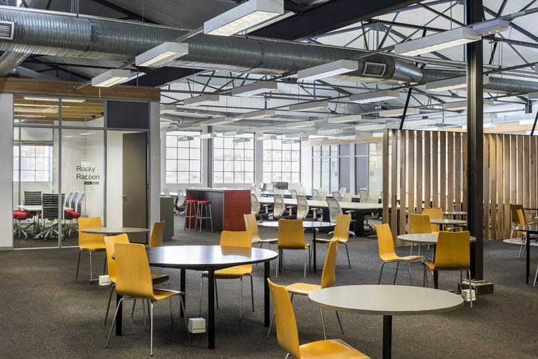 Spacious communal breakout area at 90 Maribyrnong Street with round tables and yellow chairs.