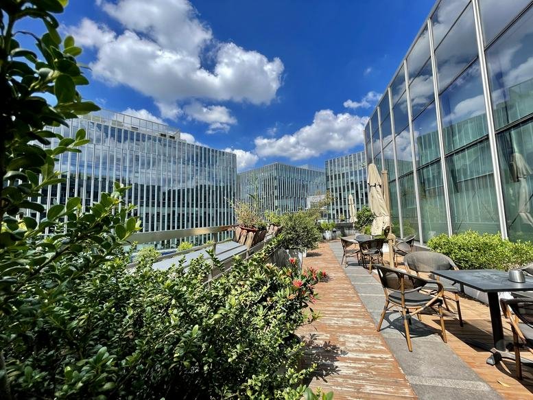 Sunny outdoor rooftop terrace at Hongqiao Vanke Center with lush greenery and dining tables.