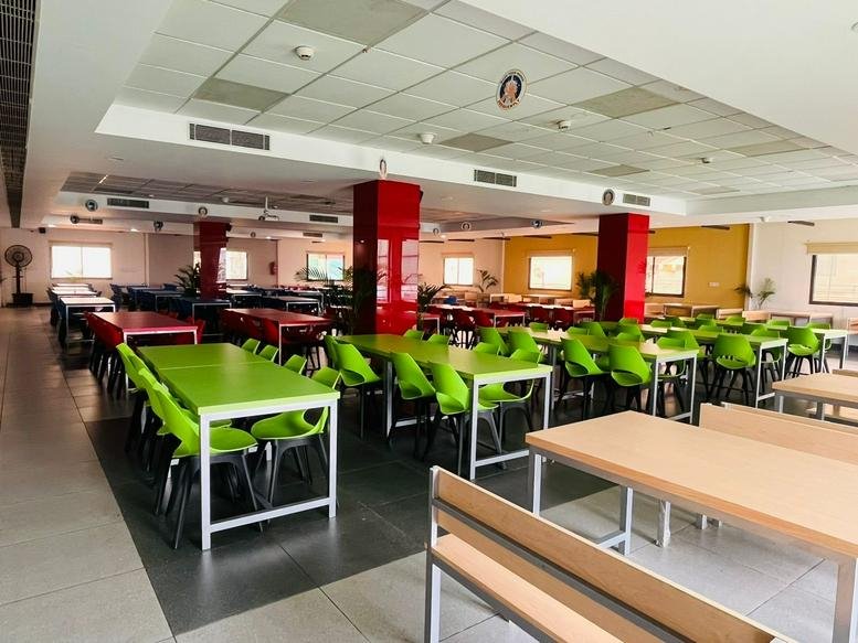 Large cafeteria with vibrant green chairs and red structural pillars.