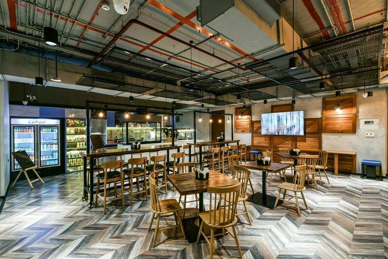 Spacious communal dining area and cafe at Abil Imperial Baner with wooden tables and industrial ceiling.