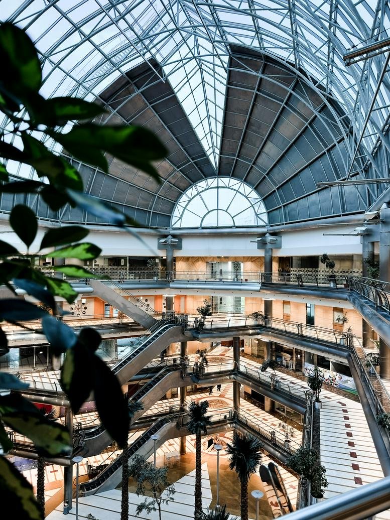Atrium view of a multi-level shopping center with glass ceilings and escalators.