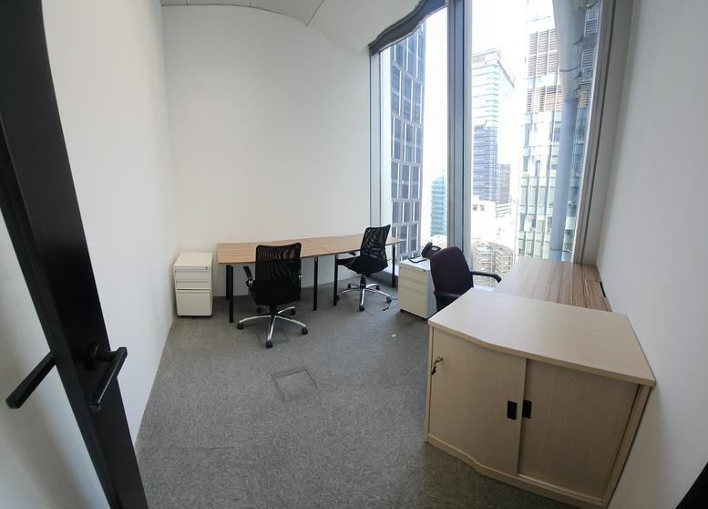 Interior view of a small office with two desks and large windows.