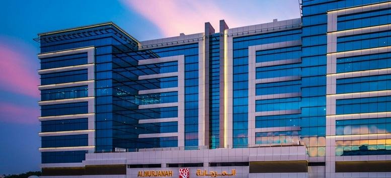 Modern glass-facade exterior of the Al Kayal, Ar Rawdah building at dusk with pink sky.