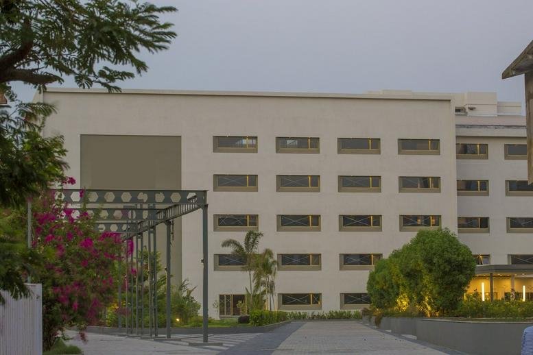 The light-colored exterior facade of Alembic City, Alembic Road, 3rd floor, Vadodara with small trees in front.