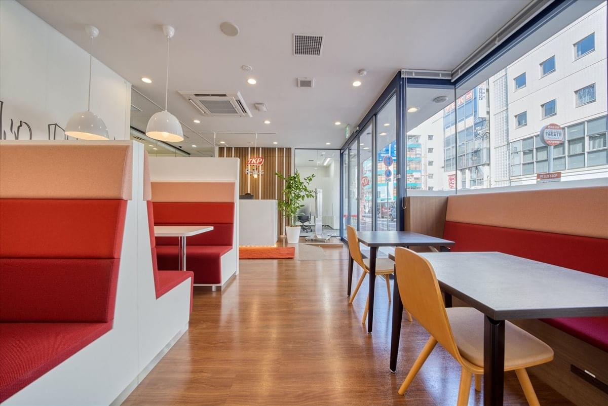 Modern coworking lounge with red cushioned booth seating and small dining tables.
