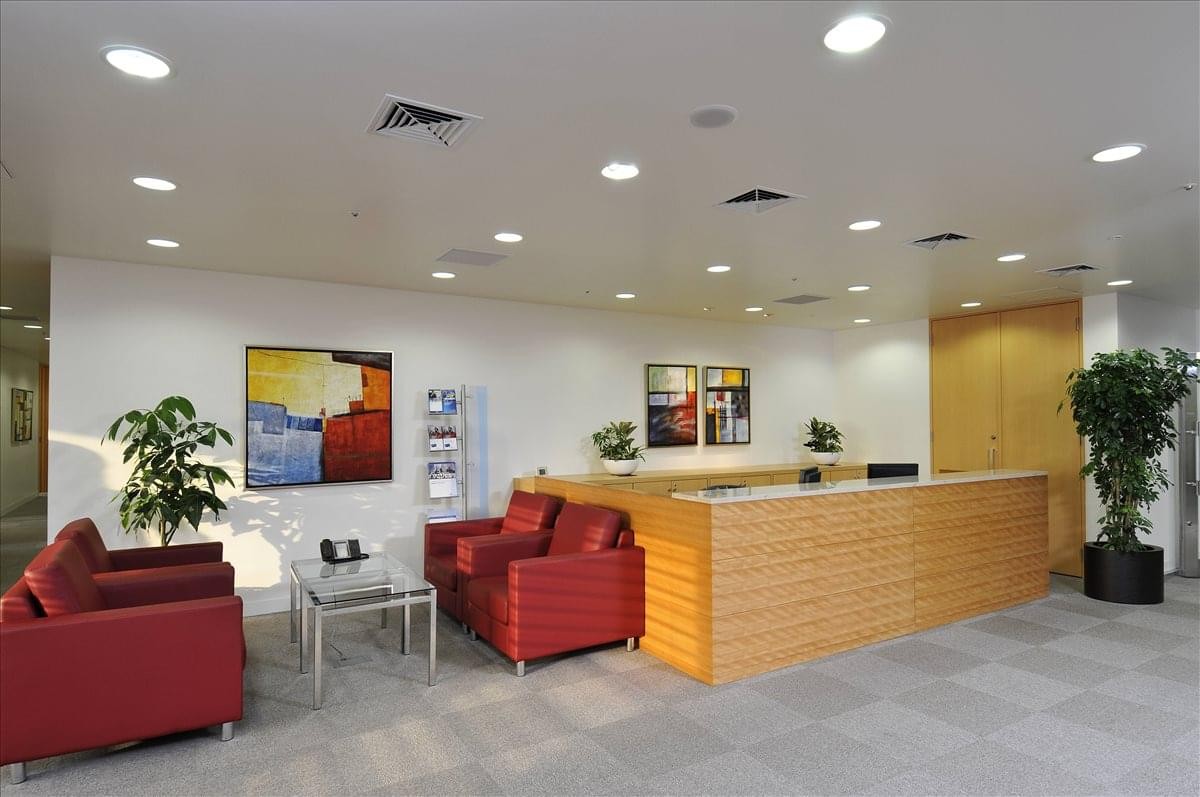 Bright reception area with wooden desk, red armchairs, and colorful wall art.