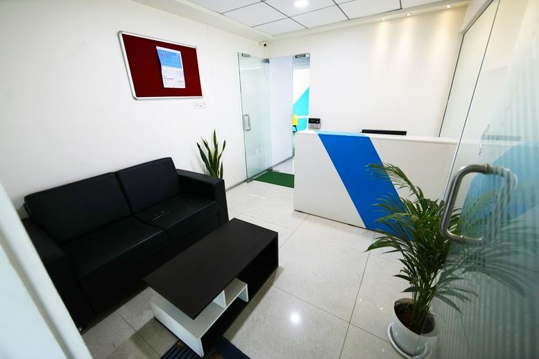 Reception area at Aspiration Building, Office No. 102 featuring a black sofa and a blue-accented desk.