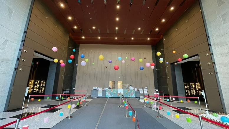 Spacious building lobby featuring high ceilings, colorful hanging ornaments, and a reception desk.
