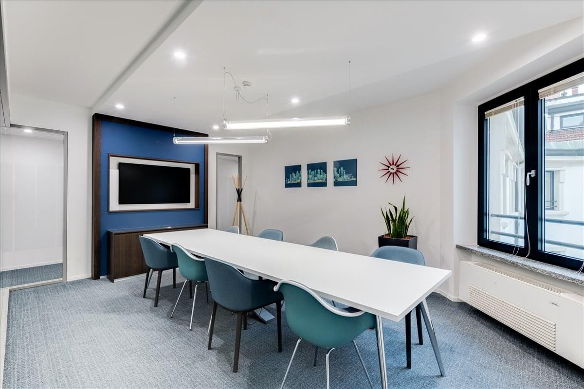 Modern conference room at Welldone, Gurugram featuring a long white table, teal chairs, and a blue accent wall.