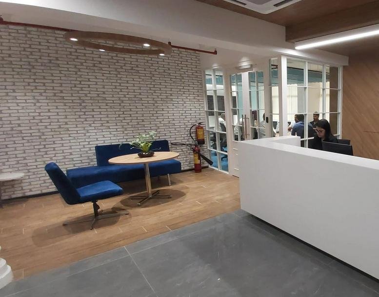Bright reception area at The Arunachal Building with blue velvet seating, white front desk, and brick feature wall.