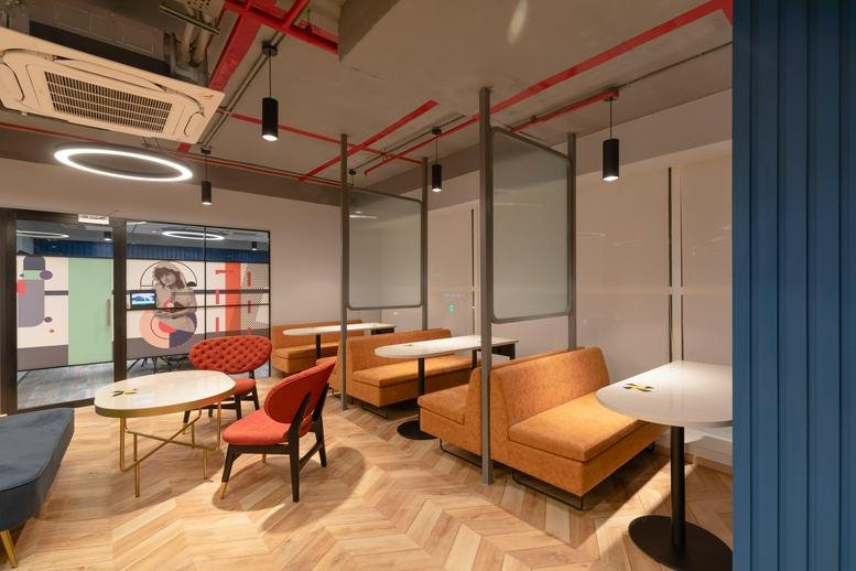 Modern breakout space at Bascon Futura SV IT Park with orange booth seating and cafe tables.