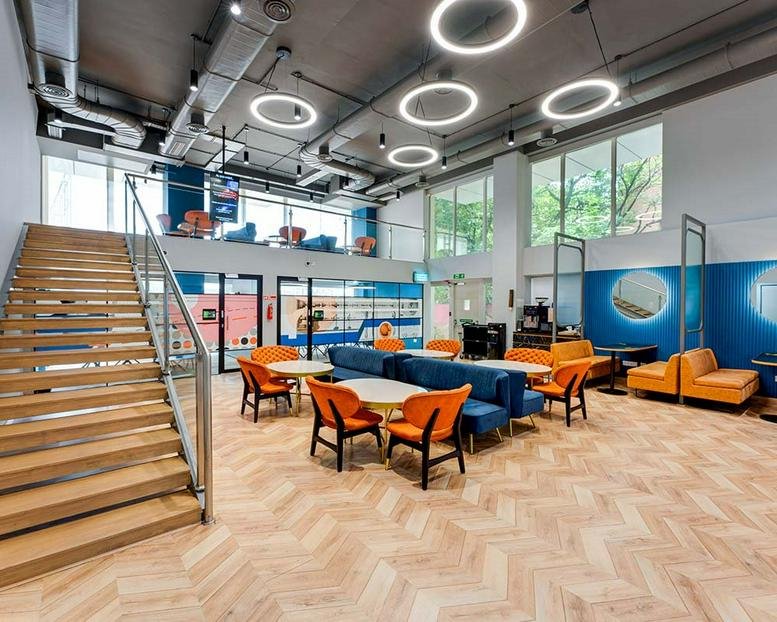 Large open-plan coworking space with colorful seating, wooden stairs, and ring-shaped ceiling lights.