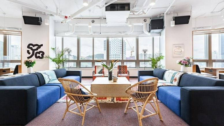 Spacious lounge area with blue sectional sofas, wicker chairs, and large windows overlooking the city.