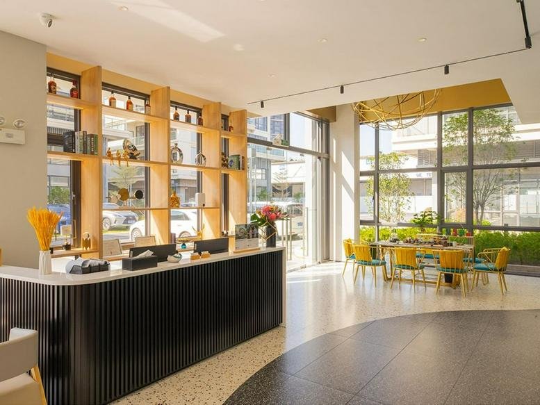 Bright reception area featuring a black slatted desk and a sunlit dining area with yellow chairs.