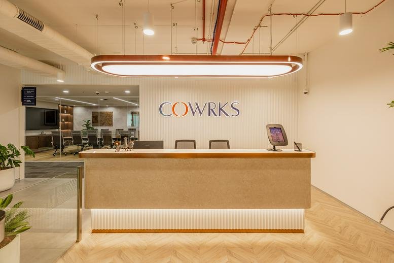 Reception desk of COWRKS BKC, Equinox Tower 4 with warm lighting and branded signage.