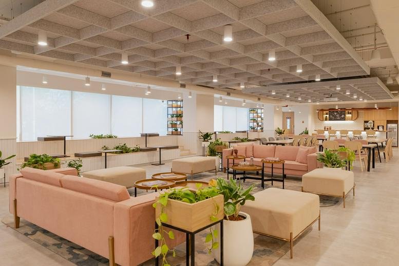 Wide-angle view of the colorful lounge at COWRKS BKC, Equinox Tower 4, with pink sofas and lush greenery.