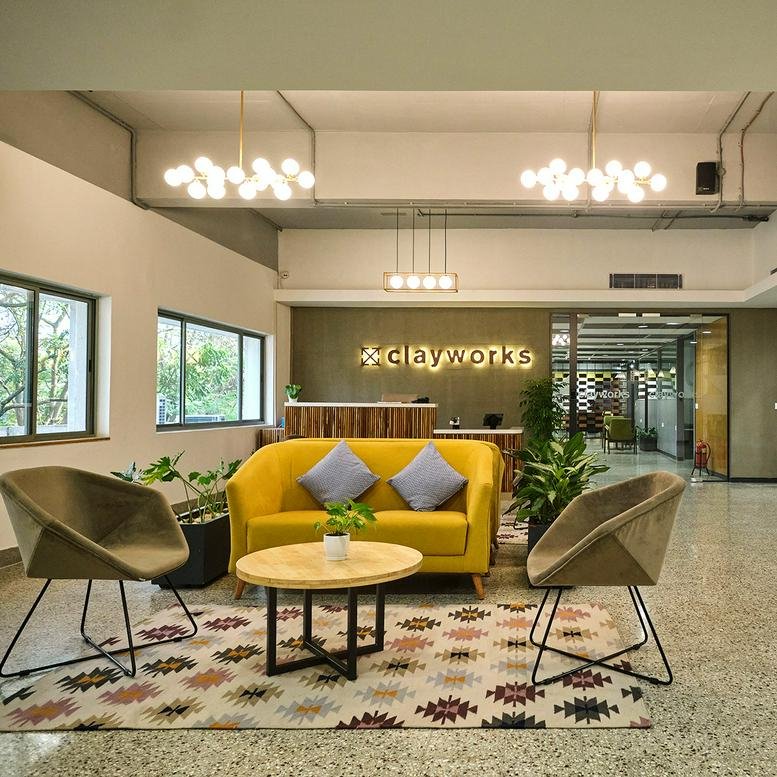 Spacious reception and lounge at Create Campus with a yellow sofa, potted plants, and modern globe chandeliers.