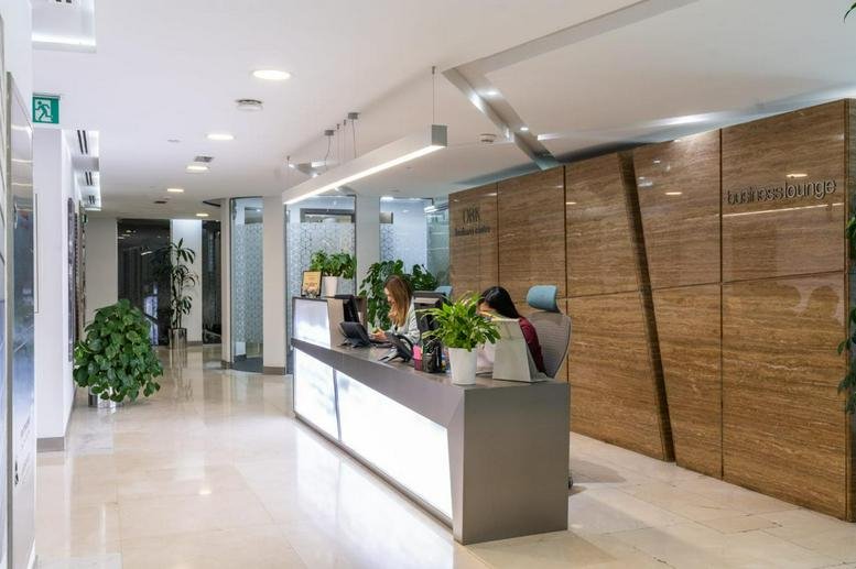 Bright reception area with a sleek desk, indoor plants, and wooden wall paneling.
