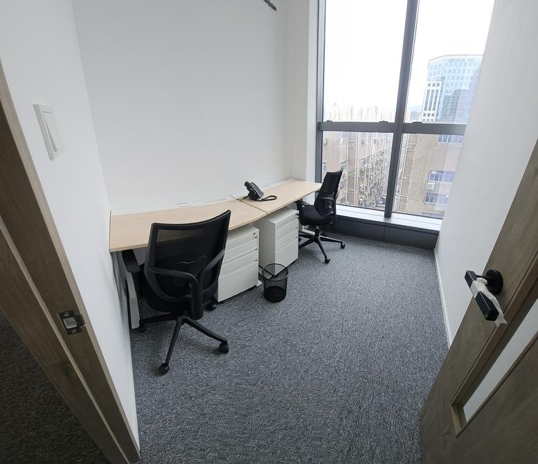 Compact two-person private office with dual desks and a large window.