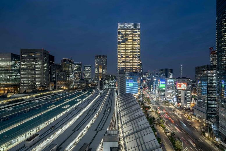 Nighttime city view of the Gran Tokyo South Tower surrounded by illuminated buildings and train tracks.