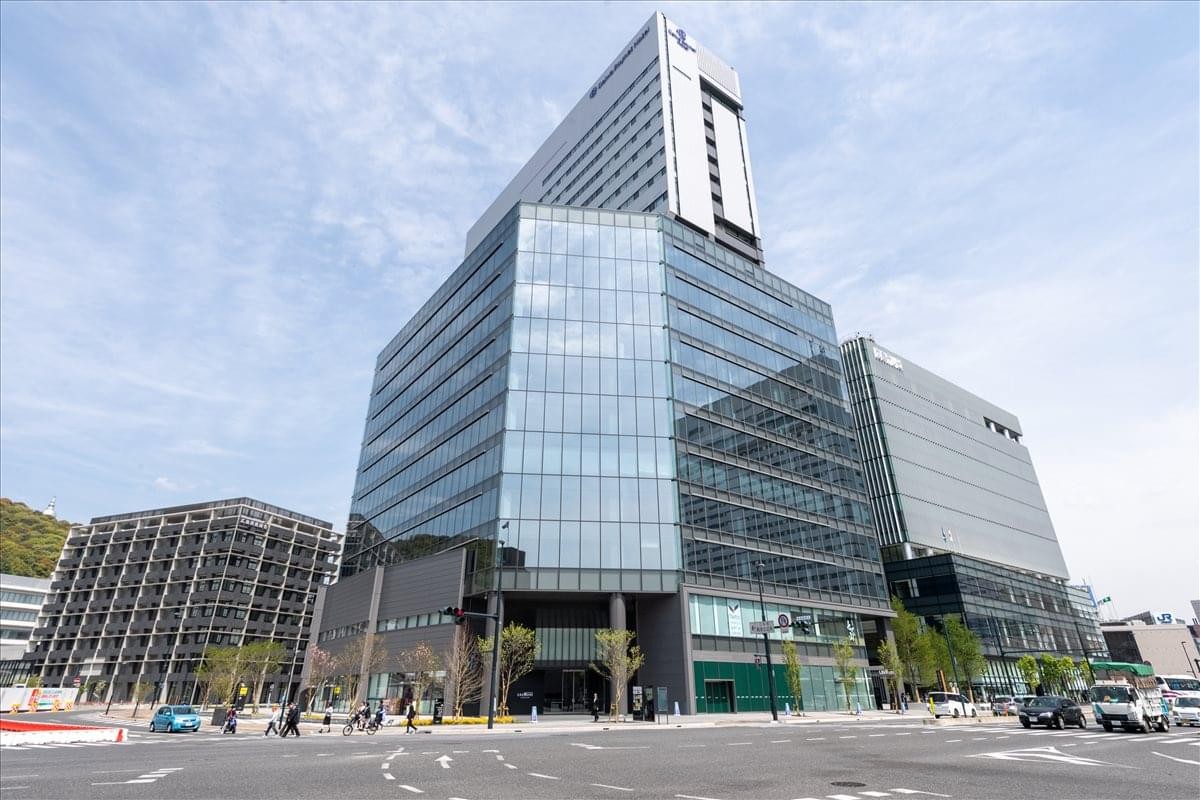 Exterior view of the glass-facade GRANODE Hiroshima 3F building under a bright blue sky.