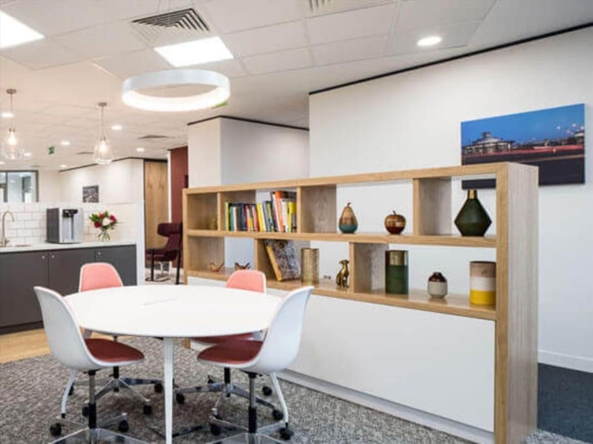 Hakata Chikushi Street Center Building communal lounge featuring a round meeting table, pink chairs, and a wooden bookshelf.